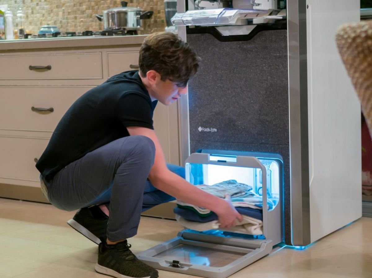 A young boy removes his impeccably folded and ironed clothes from the FoldiMate machine, offering fast, quality results. Find out how this innovative solution simplifies folding and ironing on es.foldimateofficial.com.
